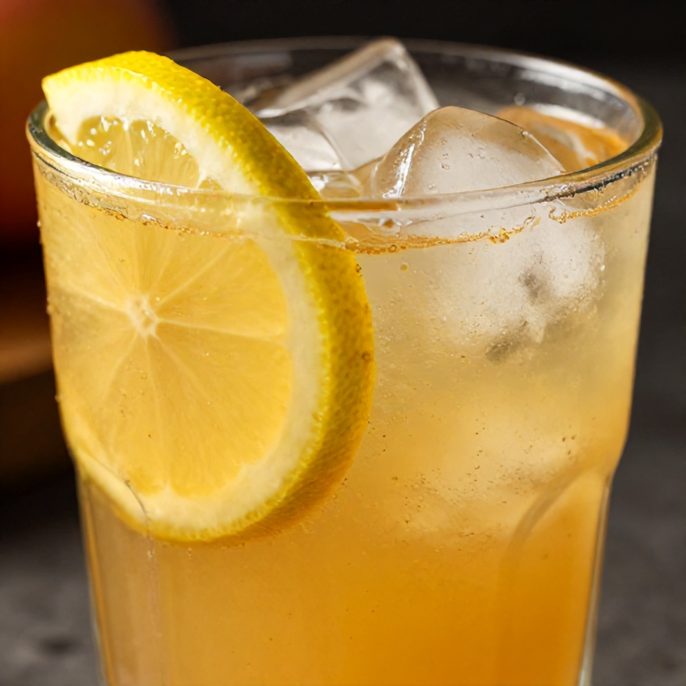 A close-up of a glass of peach ginger lemonade with a lemon slice and ice cubes